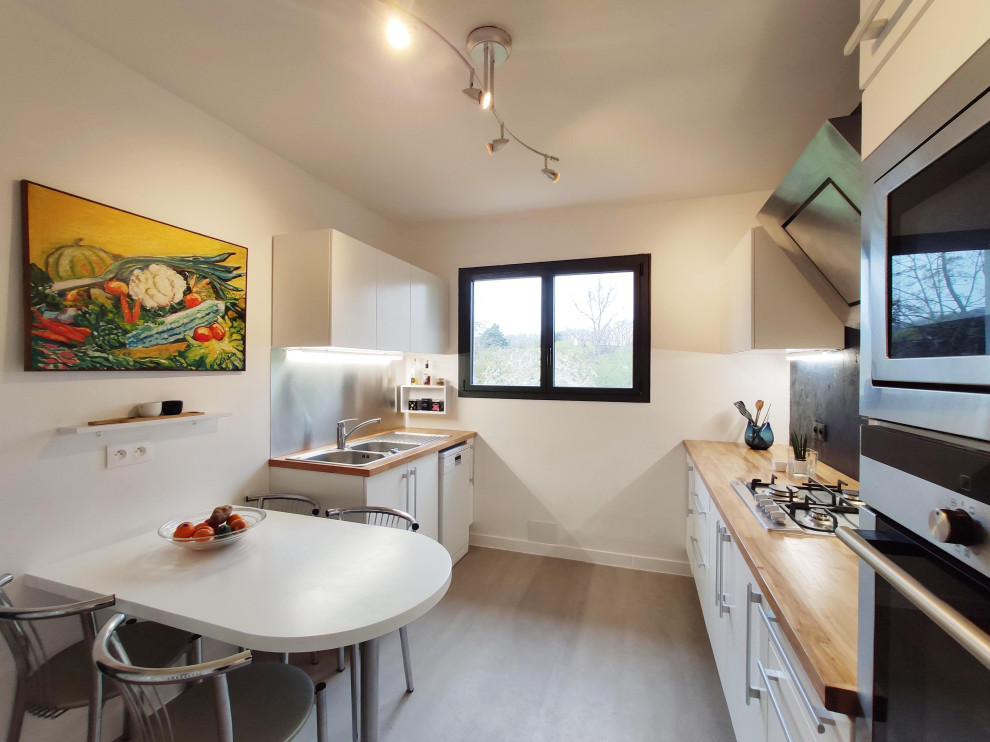 This is an example of a mid-sized contemporary galley separate kitchen in Paris with a drop-in sink, beaded inset cabinets, white cabinets, wood benchtops, metallic splashback, panelled appliances, concrete floors and grey floor.