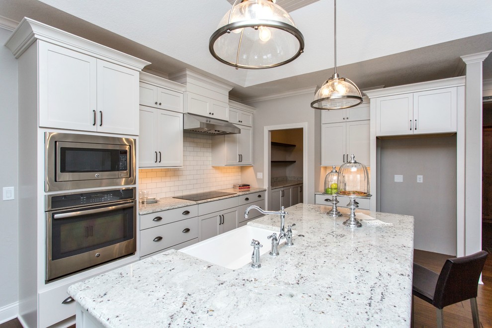 Mid-sized transitional single-wall medium tone wood floor and beige floor open concept kitchen photo with a farmhouse sink, recessed-panel cabinets, white cabinets, granite countertops, white backsplash, ceramic backsplash, stainless steel appliances and an island