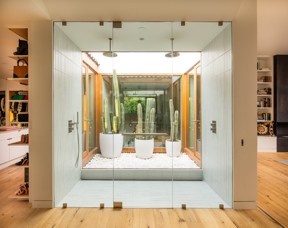 This is an example of a contemporary master bathroom in Los Angeles with a double shower, white tile, white walls, light hardwood floors, concrete benchtops, brown floor and a hinged shower door.