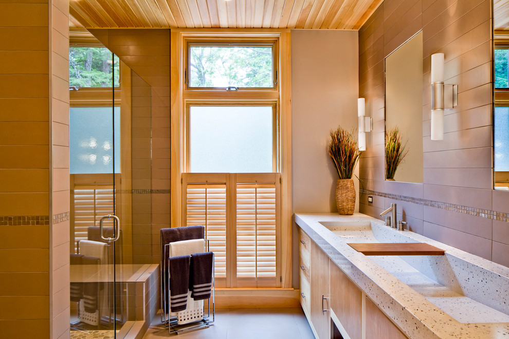 Photo of a modern master bathroom in Portland Maine with an integrated sink, flat-panel cabinets, light wood cabinets, concrete benchtops, an alcove shower, a one-piece toilet, beige tile, porcelain tile, beige walls and porcelain floors.