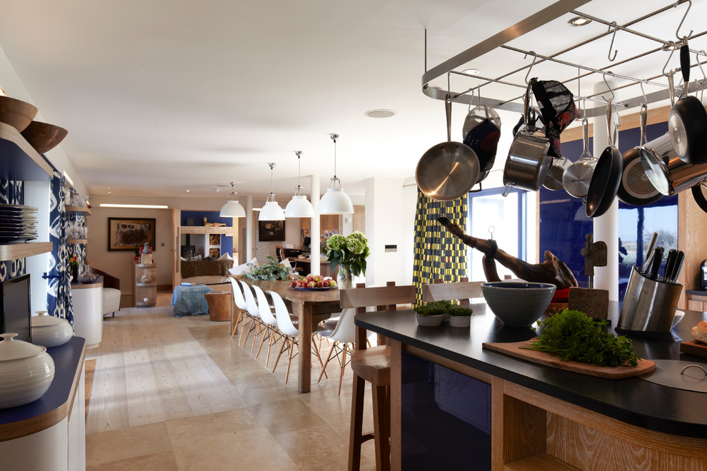 Photo of a large beach style l-shaped open plan kitchen in London with an integrated sink, flat-panel cabinets, light wood cabinets, granite benchtops, white splashback, ceramic splashback, stainless steel appliances, light hardwood floors and with island.