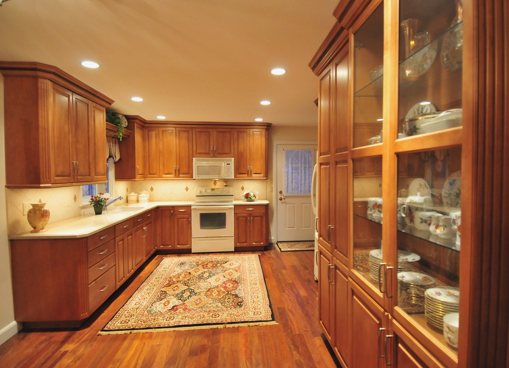 Inspiration for a mid-sized transitional medium tone wood floor eat-in kitchen remodel in New York with raised-panel cabinets, medium tone wood cabinets, solid surface countertops, ceramic backsplash, white appliances, no island, an undermount sink and beige backsplash