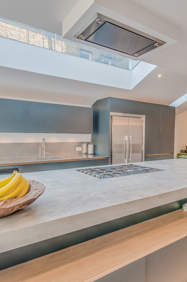 Inspiration for a mid-sized industrial galley open plan kitchen in Surrey with a single-bowl sink, flat-panel cabinets, black cabinets, concrete benchtops, metallic splashback, stainless steel appliances, concrete floors and with island.