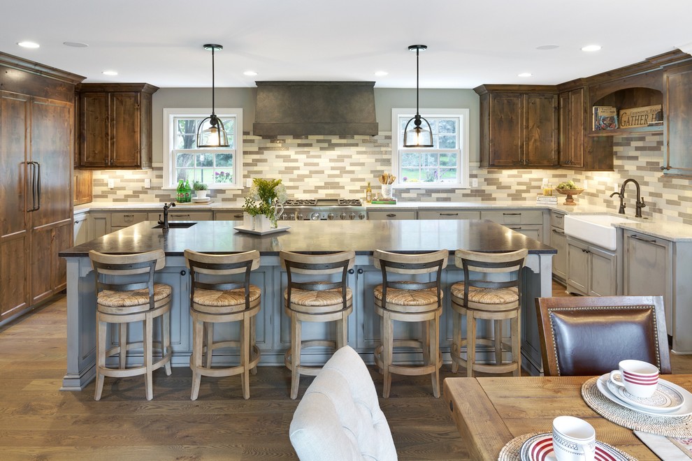 This is an example of a large country u-shaped eat-in kitchen in Minneapolis with a farmhouse sink, recessed-panel cabinets, grey cabinets, multi-coloured splashback, panelled appliances, with island, solid surface benchtops, brown floor, porcelain splashback and medium hardwood floors.