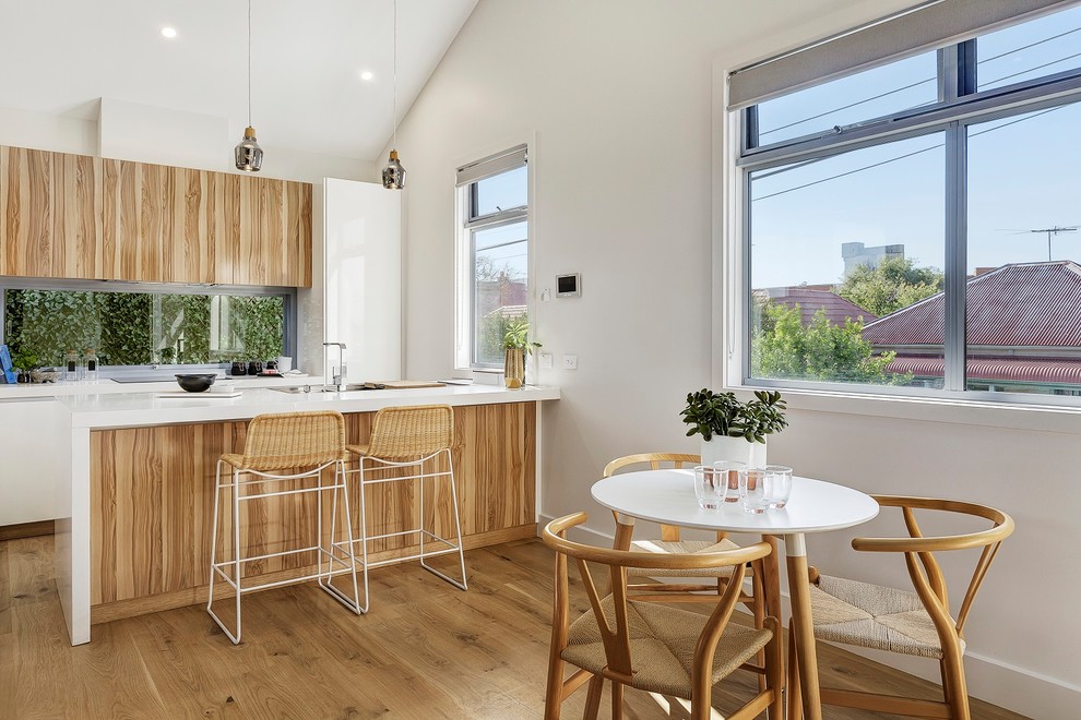 Inspiration for a scandinavian galley eat-in kitchen in Melbourne with a drop-in sink, flat-panel cabinets, medium wood cabinets, window splashback, medium hardwood floors, brown floor and white benchtop.