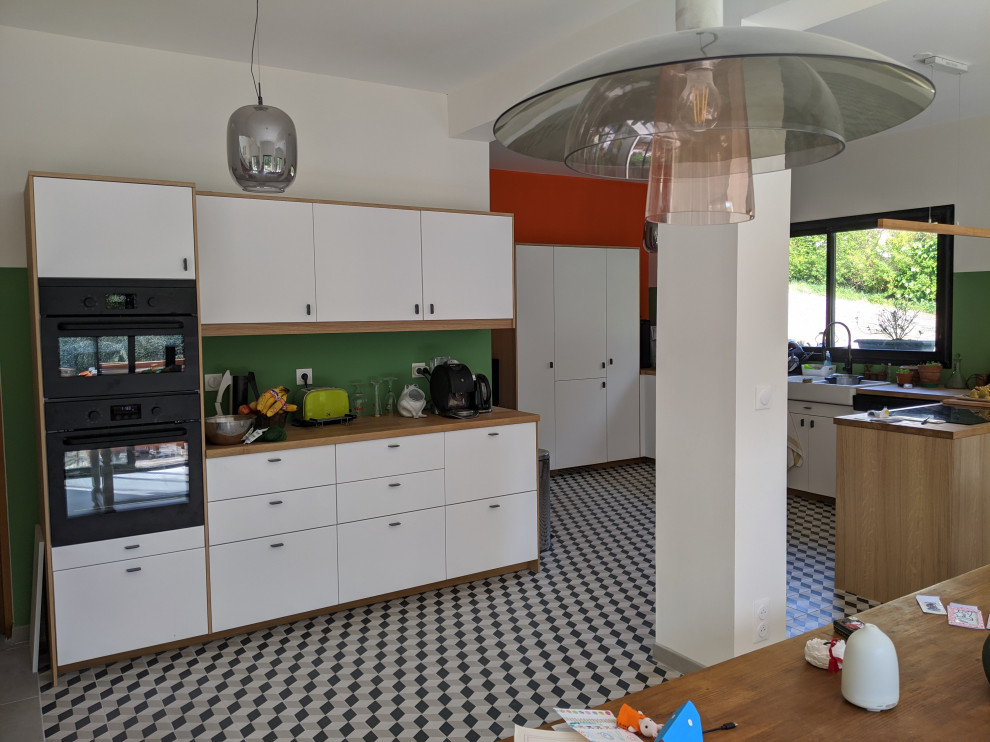 This is an example of a large contemporary l-shaped kitchen in Paris with a double-bowl sink, flat-panel cabinets, white cabinets, wood benchtops, green splashback, panelled appliances, ceramic floors, a peninsula, grey floor and beige benchtop.