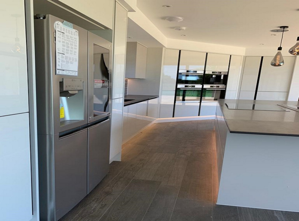 Photo of a large modern l-shaped open plan kitchen in Dorset with an integrated sink, flat-panel cabinets, white cabinets, quartzite benchtops, grey splashback, cement tile splashback, stainless steel appliances, with island and grey benchtop.