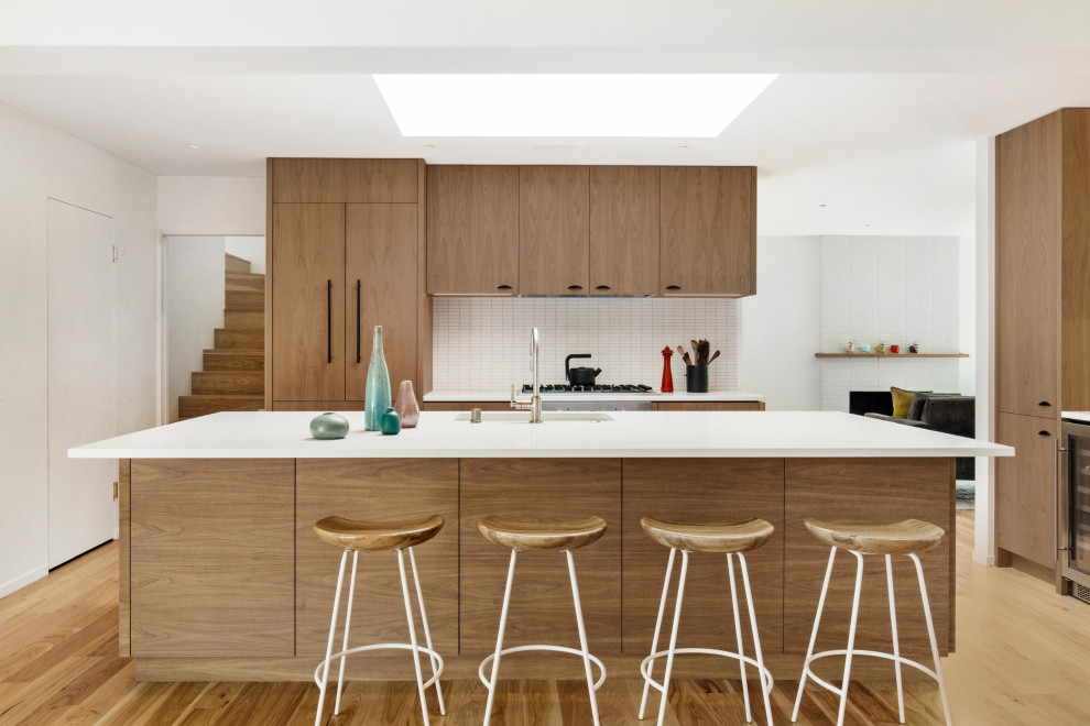 Inspiration for a midcentury kitchen in San Francisco with an integrated sink, flat-panel cabinets, medium wood cabinets, granite benchtops, white splashback, ceramic splashback, panelled appliances, light hardwood floors, with island, brown floor and white benchtop.