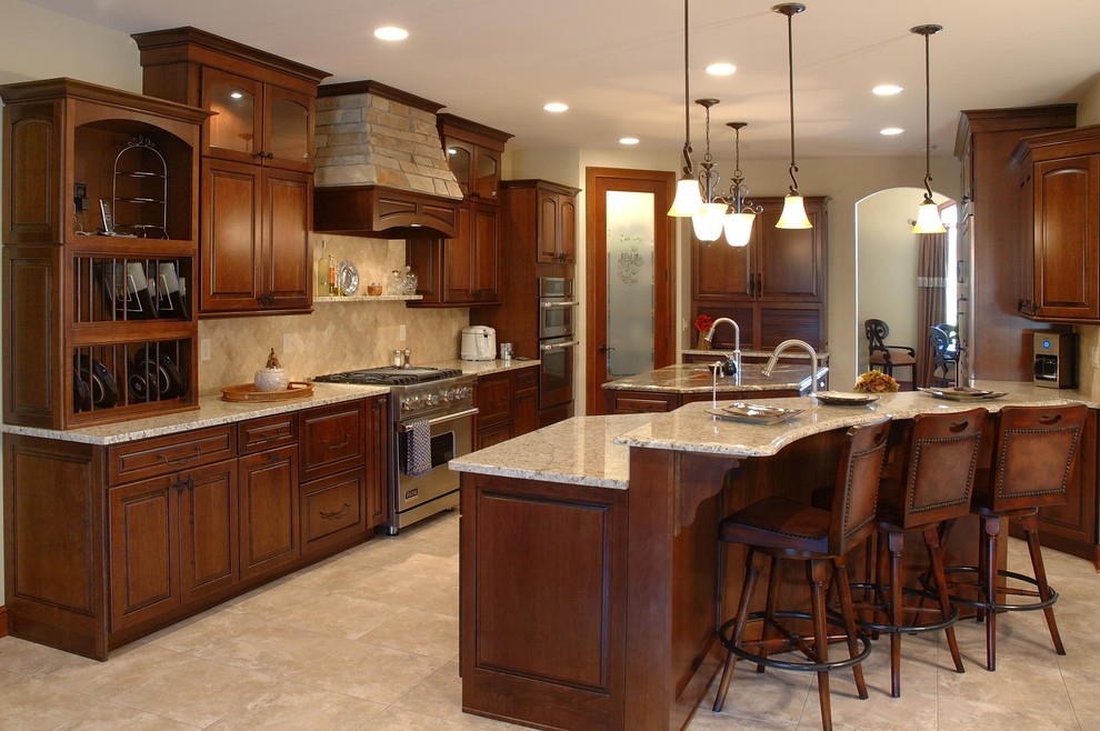 Photo of a mid-sized traditional l-shaped kitchen in Cleveland with raised-panel cabinets, limestone splashback, an undermount sink, dark wood cabinets, granite benchtops, beige splashback, stainless steel appliances, limestone floors, a peninsula, beige floor and beige benchtop.