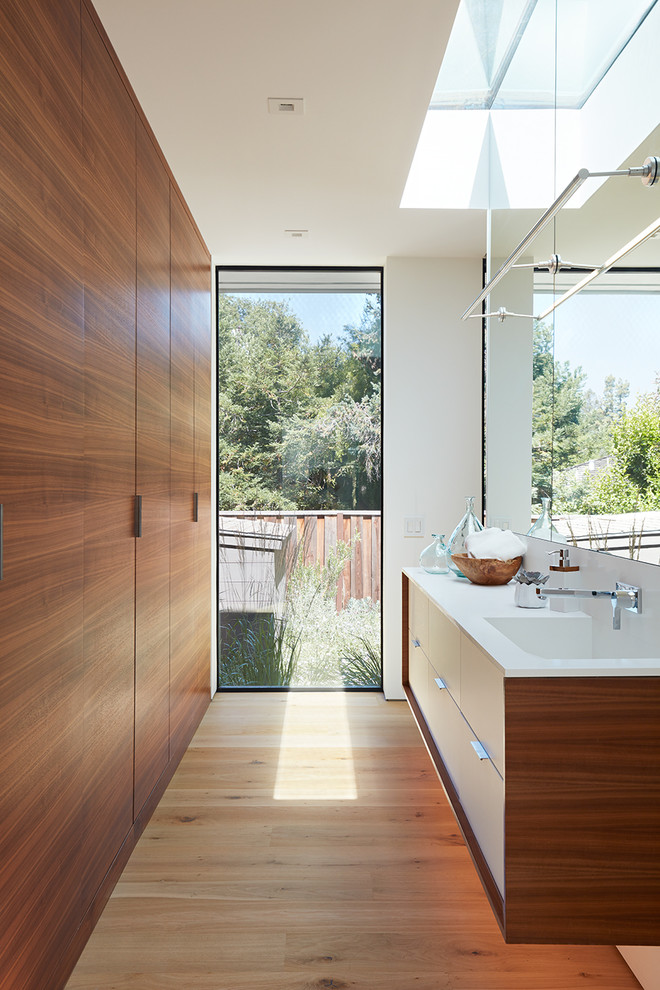 Photo of a midcentury bathroom in San Francisco with flat-panel cabinets, medium wood cabinets, white walls, light hardwood floors, an integrated sink and white benchtops.