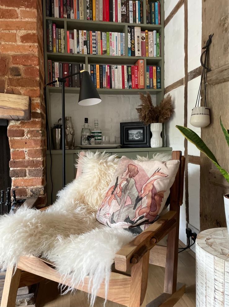 Photo of a small contemporary enclosed living room in Hertfordshire with a library, white walls, light hardwood floors, a standard fireplace, a brick fireplace surround, brown floor, exposed beam and brick walls.