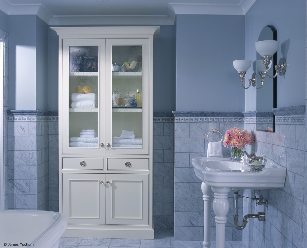 This is an example of a large traditional master bathroom in Grand Rapids with glass-front cabinets, white cabinets, a freestanding tub, gray tile, stone tile, grey walls, marble floors, a console sink and marble benchtops.