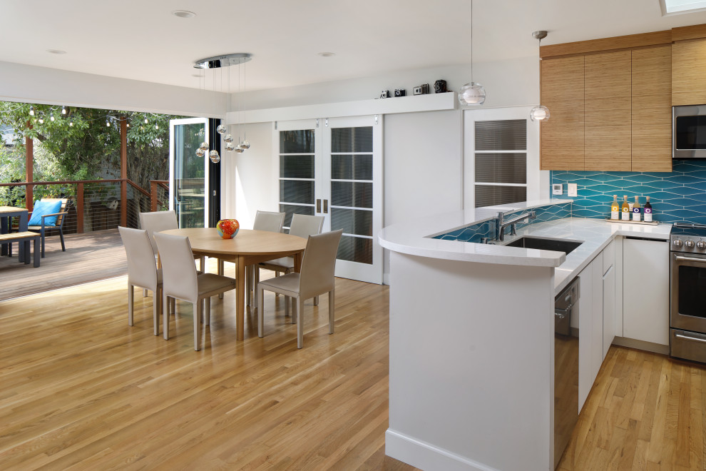 This is an example of a medium sized midcentury open plan kitchen in San Francisco with a submerged sink, flat-panel cabinets, engineered stone countertops, blue splashback, ceramic splashback, stainless steel appliances, medium hardwood flooring, a breakfast bar, brown floors and white worktops.