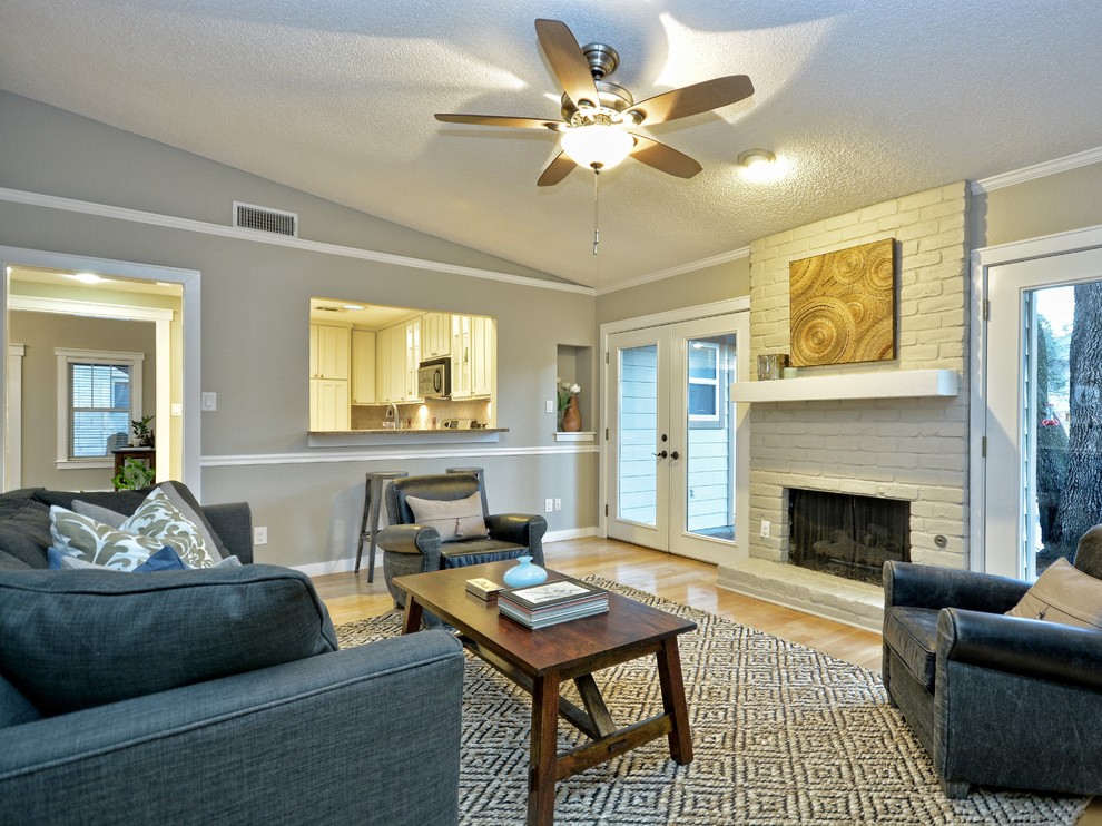 This is an example of a mid-sized arts and crafts open concept family room in Austin with grey walls, light hardwood floors, a standard fireplace and a brick fireplace surround.