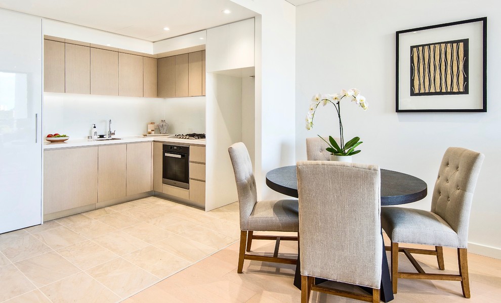 Inspiration for a small contemporary l-shaped open plan kitchen in Sydney with a single-bowl sink, flat-panel cabinets, light wood cabinets, limestone benchtops, white splashback, glass sheet splashback, stainless steel appliances, light hardwood floors and beige floor.