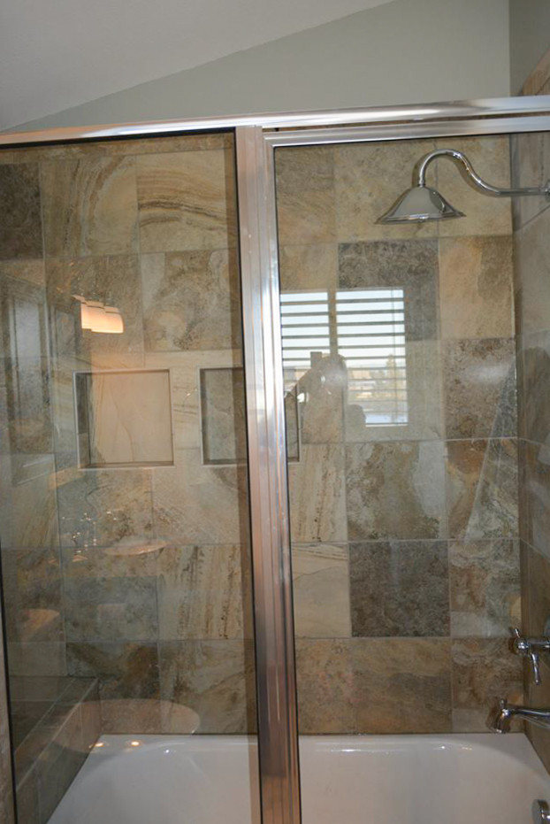 This is an example of a small transitional master bathroom in Boston with recessed-panel cabinets, brown cabinets, a shower/bathtub combo, a one-piece toilet, brown tile, ceramic tile, grey walls, ceramic floors, a drop-in sink, granite benchtops, beige floor, a sliding shower screen and beige benchtops.