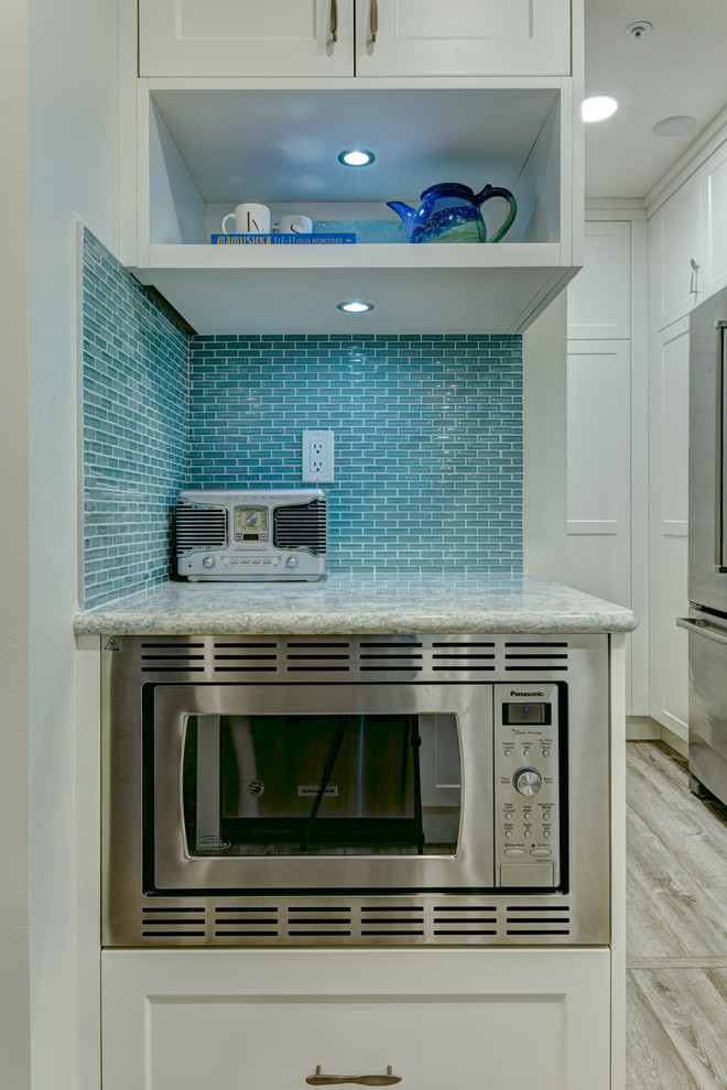 This is an example of a small eclectic u-shaped eat-in kitchen in Vancouver with an undermount sink, shaker cabinets, white cabinets, quartz benchtops, blue splashback, mosaic tile splashback, stainless steel appliances and a peninsula.
