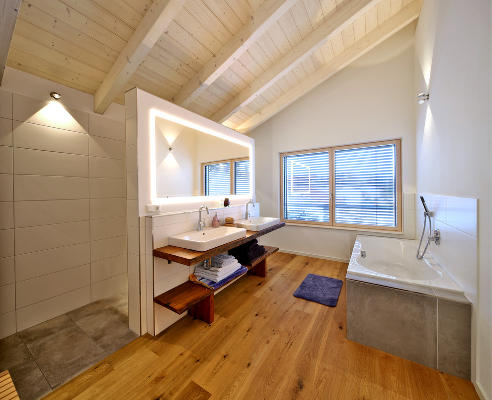This is an example of a mid-sized country master wet room bathroom in Munich with open cabinets, a drop-in tub, gray tile, a vessel sink, wood benchtops, an open shower, brown benchtops, white walls, medium hardwood floors, brown floor and dark wood cabinets.