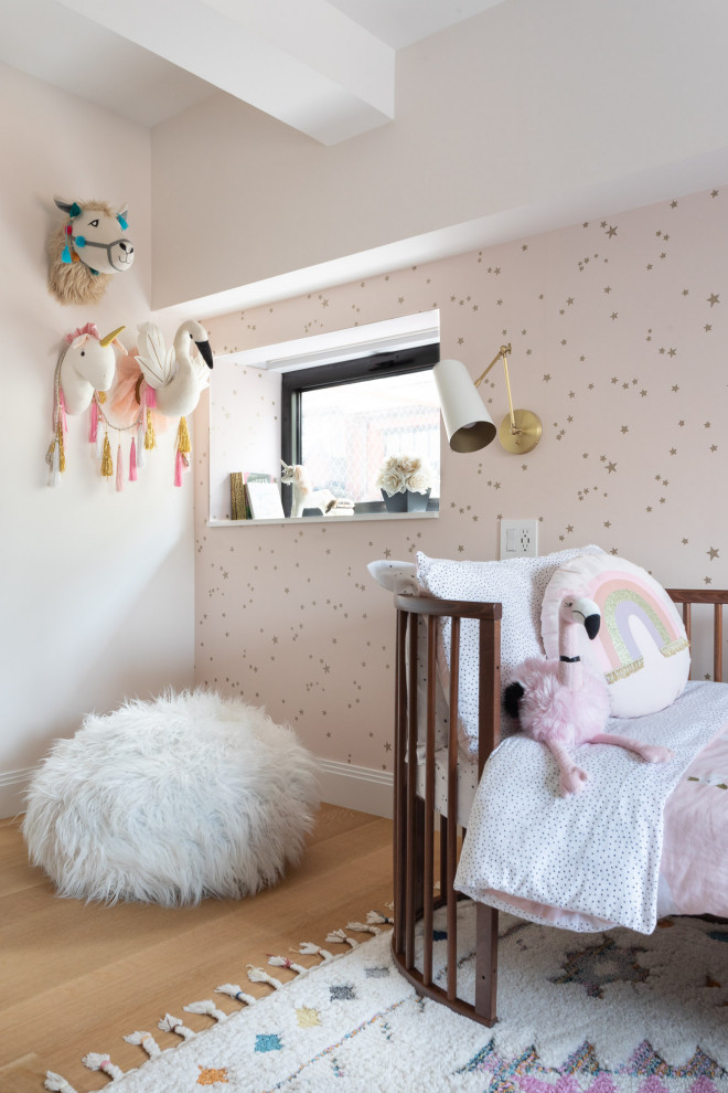This is an example of a small transitional kids' room in New York with pink walls, light hardwood floors, brown floor and wallpaper.