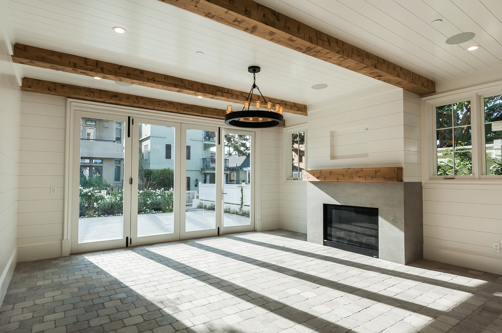 Large beach style open concept family room in San Diego with white walls, limestone floors, a standard fireplace, a concrete fireplace surround, a wall-mounted tv and grey floor.