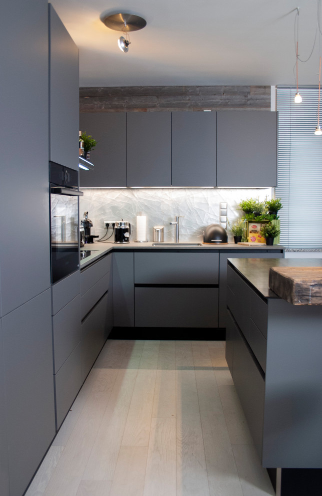 Design ideas for a small industrial l-shaped eat-in kitchen in Munich with an undermount sink, flat-panel cabinets, grey cabinets, granite benchtops, metallic splashback, black appliances, light hardwood floors, with island and grey benchtop.