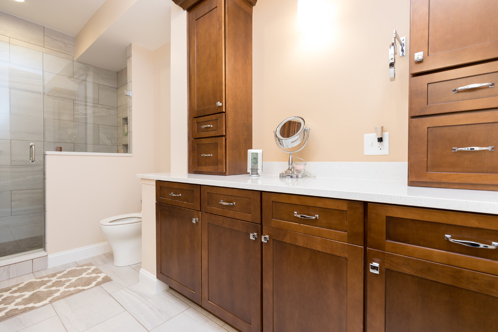 Mid-sized transitional master bathroom in DC Metro with shaker cabinets, dark wood cabinets, an open shower, a one-piece toilet, gray tile, ceramic tile, beige walls, ceramic floors, a vessel sink, engineered quartz benchtops, grey floor and a hinged shower door.