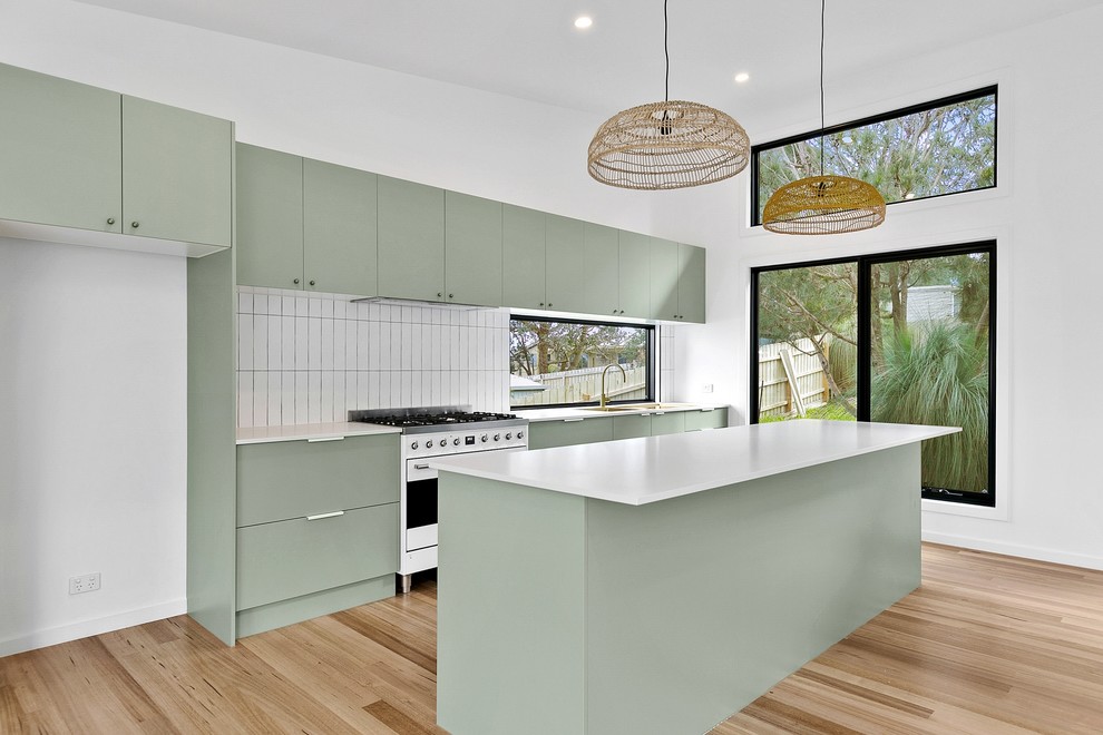 Inspiration for a medium sized contemporary galley open plan kitchen in Melbourne with a double-bowl sink, flat-panel cabinets, green cabinets, engineered stone countertops, white splashback, metro tiled splashback, white appliances, medium hardwood flooring, an island and white worktops.