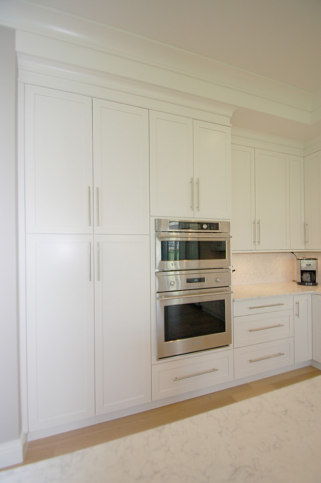 This is an example of a mid-sized transitional l-shaped eat-in kitchen in New York with an undermount sink, recessed-panel cabinets, white cabinets, quartz benchtops, white splashback, stone slab splashback, panelled appliances, light hardwood floors and with island.