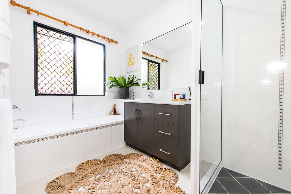 Photo of a beach style master bathroom in Brisbane with flat-panel cabinets, brown cabinets, an alcove tub, a corner shower, white tile, white walls, a drop-in sink, black floor, a hinged shower door and white benchtops.