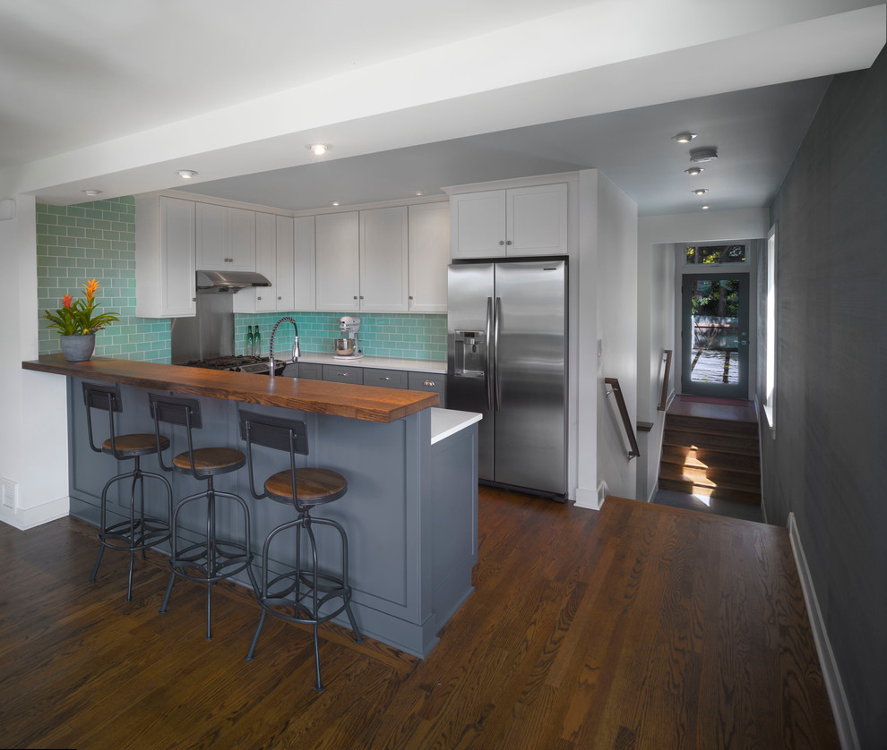 Design ideas for a mid-sized eclectic u-shaped eat-in kitchen in Seattle with yellow cabinets, quartz benchtops, green splashback, glass tile splashback, stainless steel appliances and medium hardwood floors.