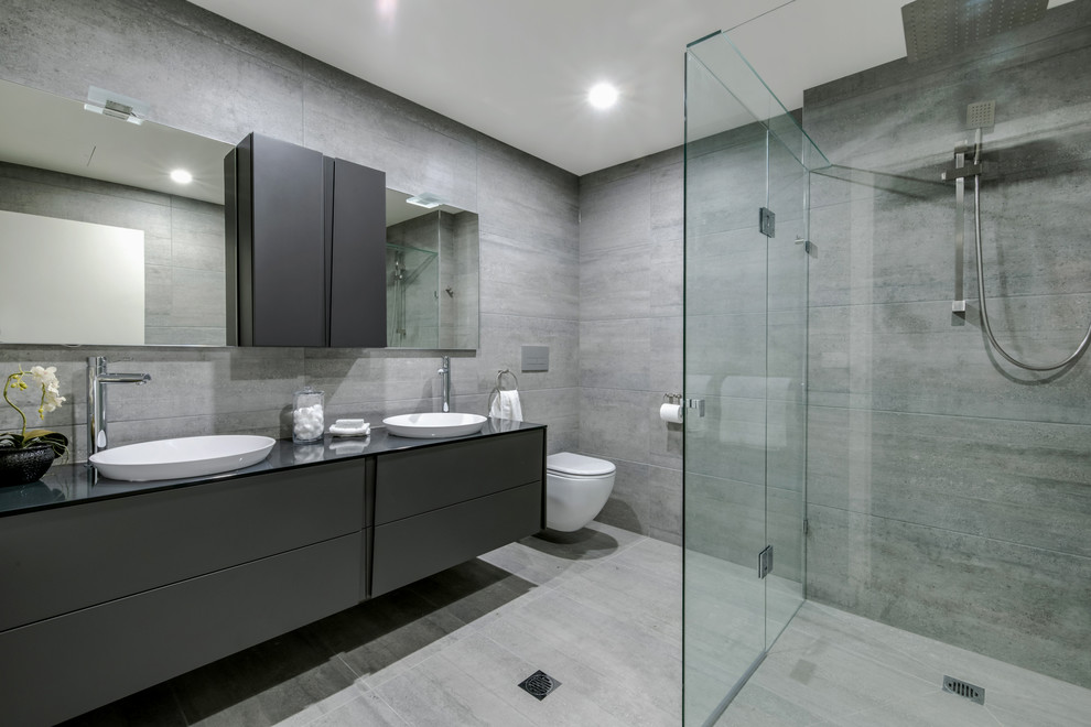 Photo of a mid-sized modern bathroom in Melbourne with raised-panel cabinets, grey cabinets, a freestanding tub, an alcove shower, a one-piece toilet, gray tile, ceramic tile, ceramic floors, a drop-in sink and glass benchtops.