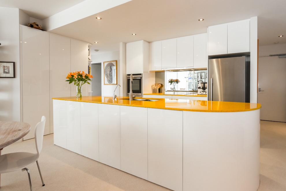 Design ideas for a small contemporary galley open plan kitchen in Perth with an undermount sink, flat-panel cabinets, white cabinets, metallic splashback, glass sheet splashback, stainless steel appliances, with island and recycled glass benchtops.