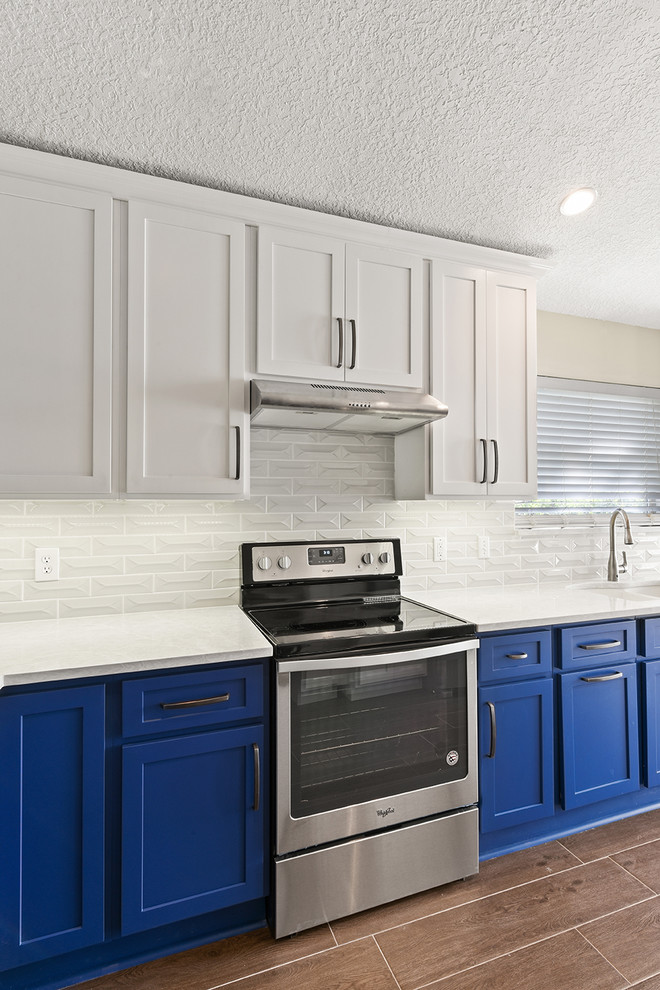 Open concept kitchen - large transitional l-shaped vinyl floor and brown floor open concept kitchen idea in Jacksonville with an undermount sink, shaker cabinets, blue cabinets, quartzite countertops, white backsplash, ceramic backsplash, stainless steel appliances and a peninsula