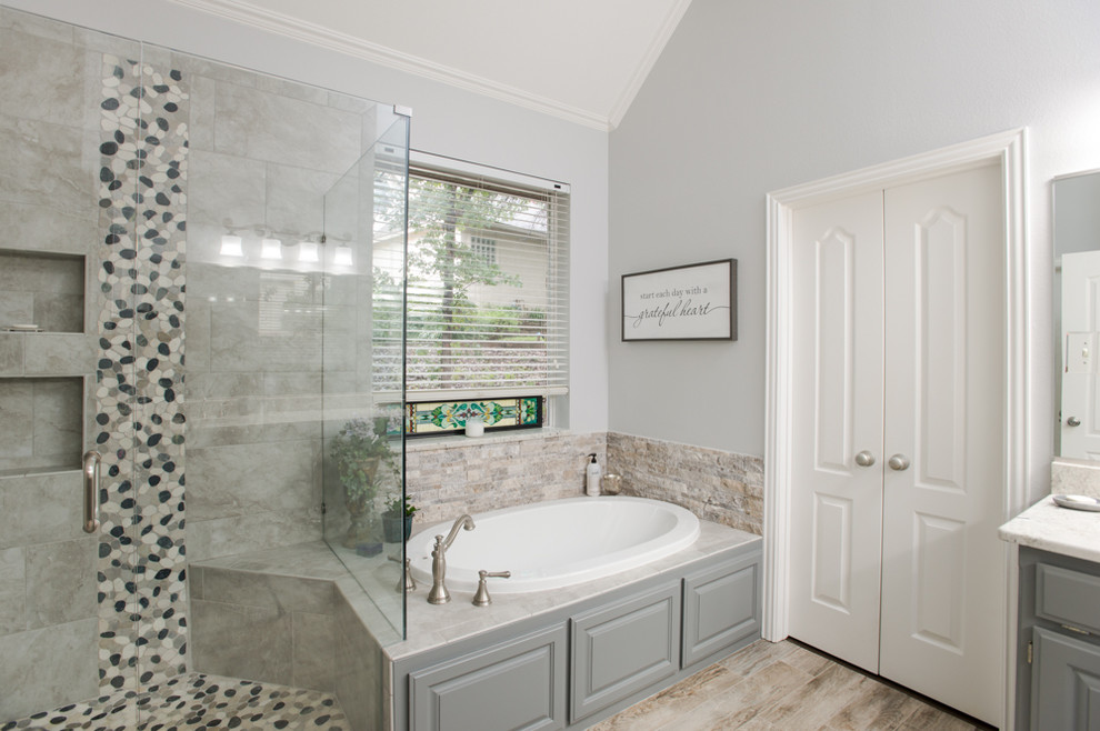 Mid-sized country master bathroom in Dallas with raised-panel cabinets, grey cabinets, a drop-in tub, an alcove shower, a two-piece toilet, gray tile, porcelain tile, grey walls, porcelain floors, an undermount sink, granite benchtops, grey floor, a hinged shower door and white benchtops.