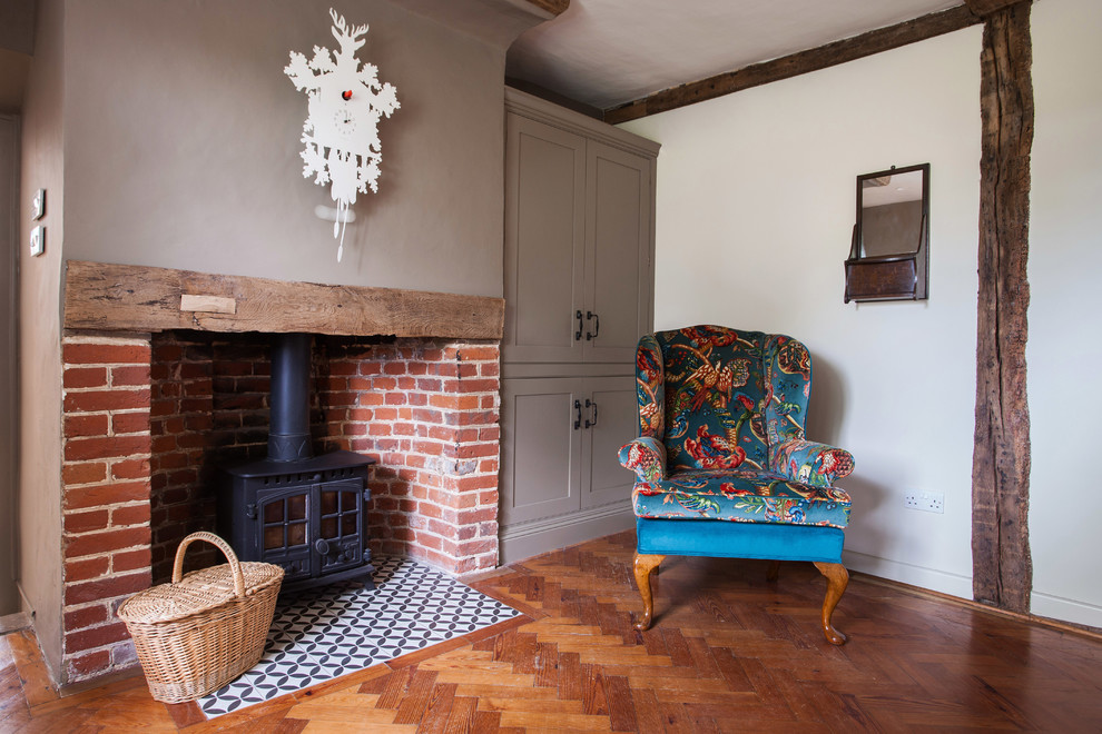 Mid-sized country enclosed living room in Kent with a library, beige walls, dark hardwood floors, a wood stove, a brick fireplace surround and multi-coloured floor.