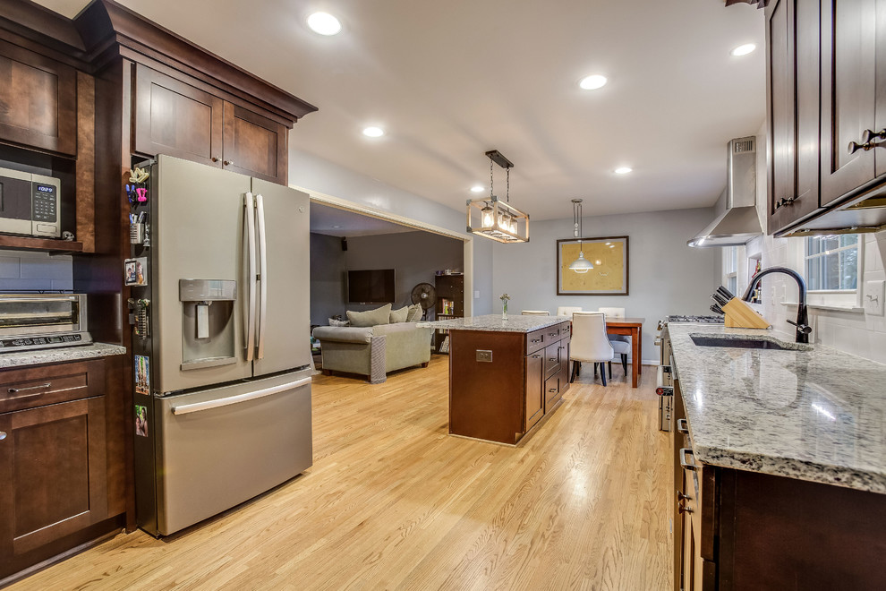 Example of a mid-sized transitional l-shaped light wood floor and yellow floor eat-in kitchen design in Birmingham with a double-bowl sink, shaker cabinets, dark wood cabinets, granite countertops, white backsplash, subway tile backsplash, stainless steel appliances, an island and gray countertops