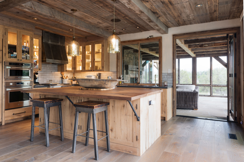 Photo of a country l-shaped kitchen in Other with shaker cabinets, medium wood cabinets, wood benchtops, grey splashback, stainless steel appliances, medium hardwood floors, with island, brown floor and brown benchtop.