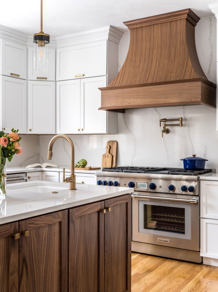 Bild på ett vintage vit vitt u-kök, med en undermonterad diskho, luckor med infälld panel, vita skåp, bänkskiva i kvarts, vitt stänkskydd, rostfria vitvaror, mellanmörkt trägolv, en köksö och brunt golv