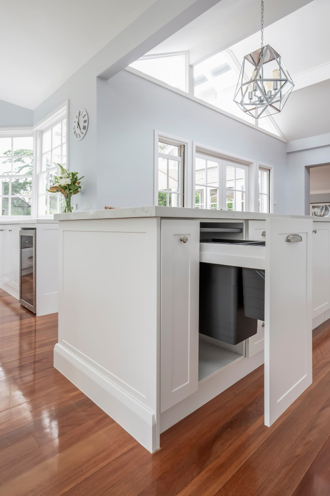 Large transitional u-shaped medium tone wood floor, brown floor and exposed beam kitchen pantry photo in Sydney with a farmhouse sink, shaker cabinets, white cabinets, quartz countertops, white backsplash, subway tile backsplash, stainless steel appliances, two islands and white countertops