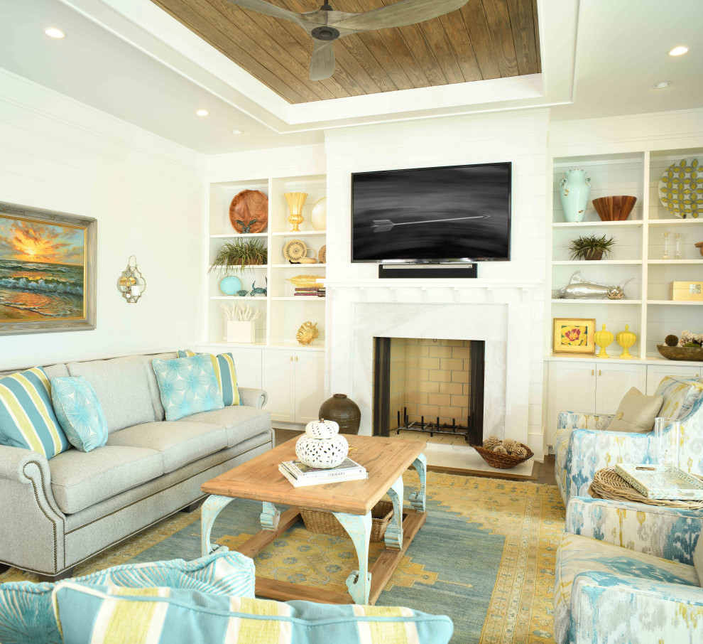 Beach style living room in Charleston with white walls, medium hardwood floors, a standard fireplace, a stone fireplace surround, a wall-mounted tv, brown floor and planked wall panelling.