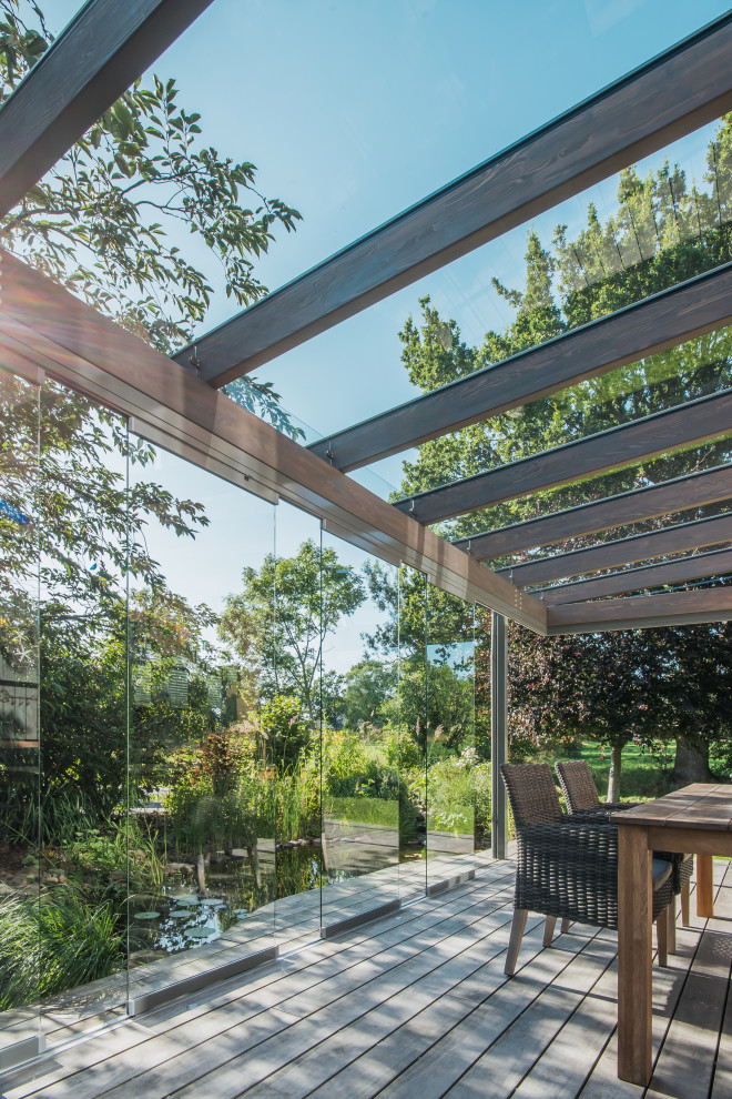 Ispirazione per una terrazza minimal di medie dimensioni, nel cortile laterale e a piano terra con con illuminazione, un parasole e parapetto in vetro