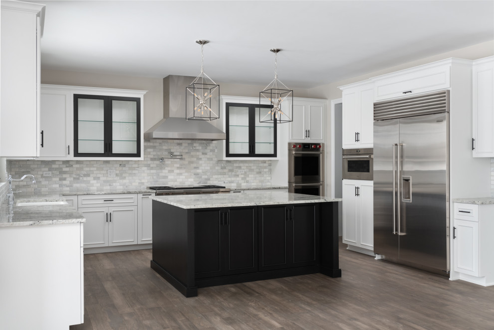 Photo of an expansive modern u-shaped open plan kitchen in Chicago with a farmhouse sink, white cabinets, grey splashback, stainless steel appliances, medium hardwood floors, with island, stone tile splashback, brown floor, white benchtop, granite benchtops and recessed-panel cabinets.