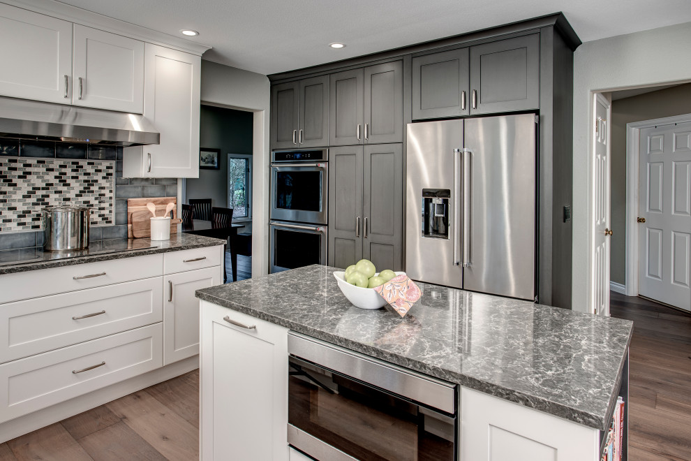 Inspiration for a mid-sized transitional l-shaped medium tone wood floor and brown floor eat-in kitchen remodel in Seattle with a double-bowl sink, shaker cabinets, gray cabinets, quartz countertops, gray backsplash, ceramic backsplash, stainless steel appliances, two islands and gray countertops