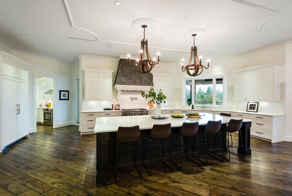 Example of a huge mountain style u-shaped medium tone wood floor and brown floor open concept kitchen design in Vancouver with an undermount sink, shaker cabinets, white cabinets, solid surface countertops, white backsplash, stone slab backsplash, stainless steel appliances, an island and white countertops
