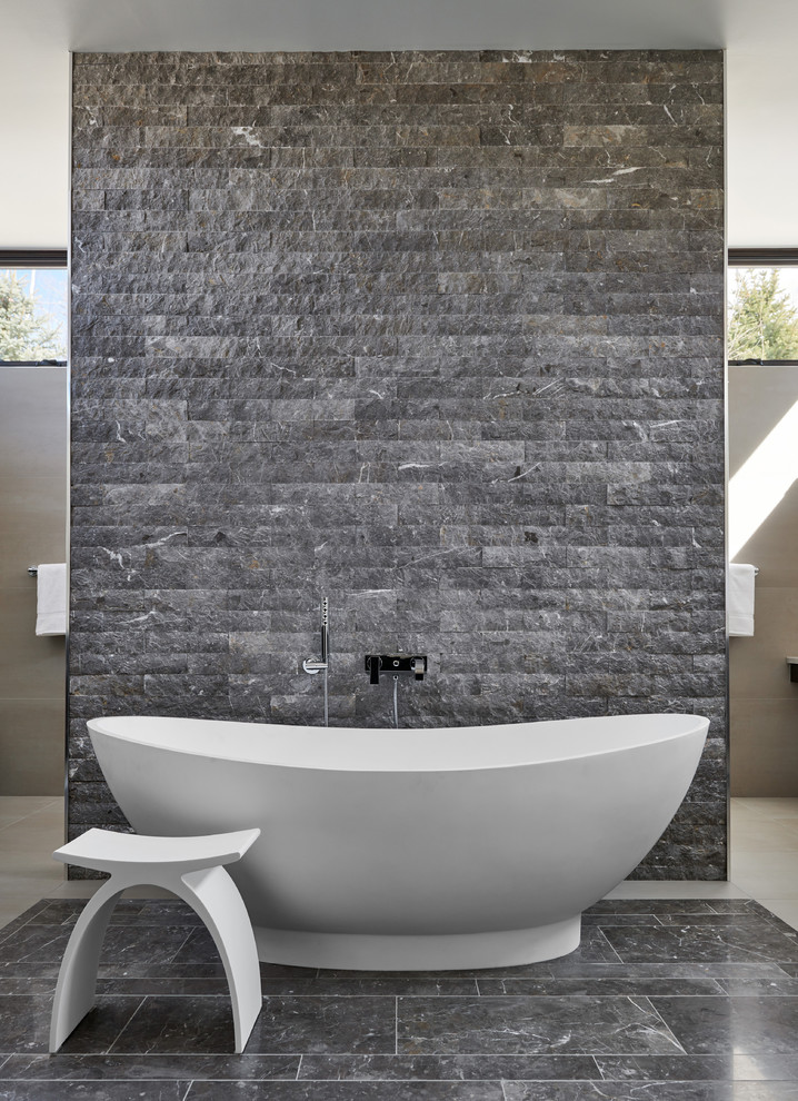 This is an example of a mid-sized modern master bathroom in Denver with a freestanding tub, beige walls, an open shower, gray tile, stone tile, limestone floors, grey floor and an open shower.