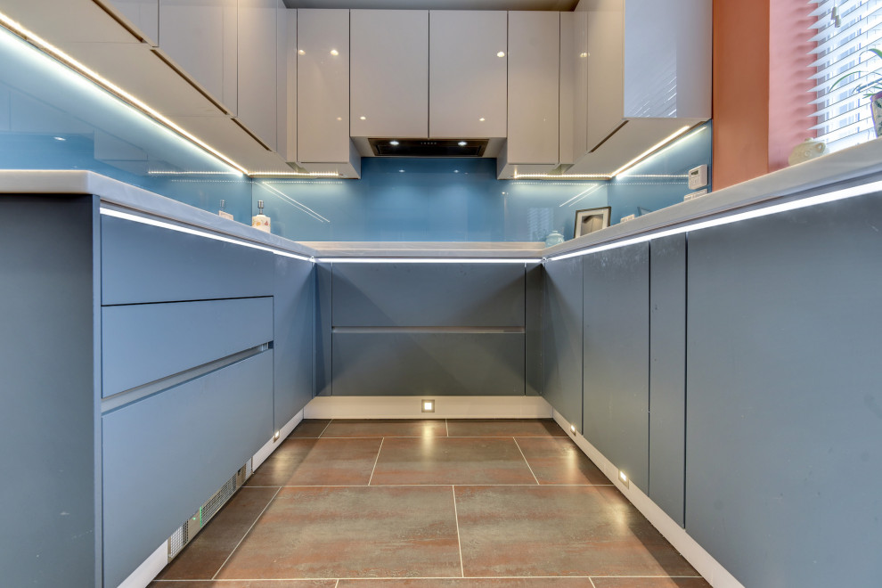 Inspiration for a large modern grey and teal u-shaped kitchen/diner in Sussex with a built-in sink, flat-panel cabinets, blue cabinets, composite countertops, blue splashback, glass sheet splashback, integrated appliances, vinyl flooring, no island, brown floors, white worktops and feature lighting.