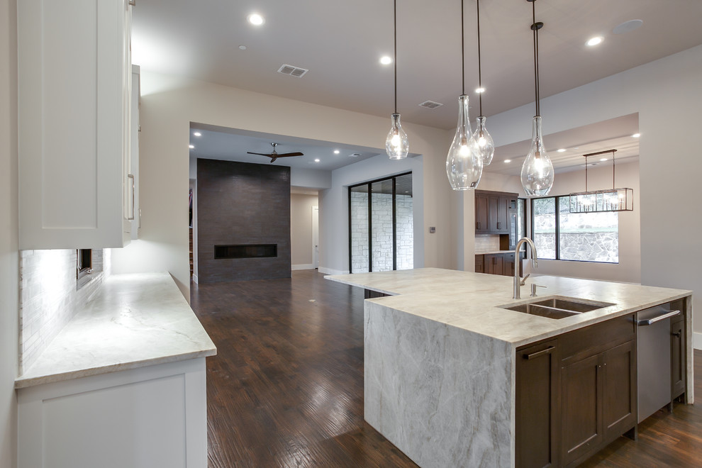 Large transitional l-shaped open plan kitchen in Dallas with a double-bowl sink, shaker cabinets, white cabinets, granite benchtops, grey splashback, stone tile splashback, stainless steel appliances, medium hardwood floors, with island and brown floor.