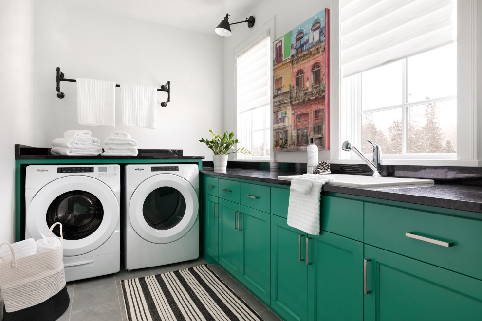 Inspiration for a mid-sized contemporary l-shaped dedicated laundry room in Minneapolis with recessed-panel cabinets, green cabinets, granite benchtops, white walls, ceramic floors, a side-by-side washer and dryer, grey floor, black benchtop and a drop-in sink.