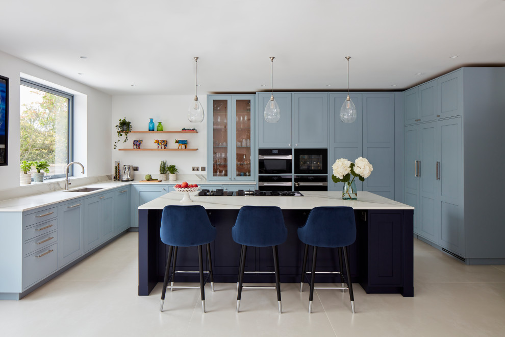 This is an example of a large traditional u-shaped kitchen in London with shaker cabinets, an island, a submerged sink, blue cabinets, marble worktops, white splashback, marble splashback, integrated appliances, beige floors and white worktops.