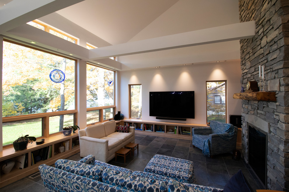 Стильный дизайн: большая открытая гостиная комната в стиле модернизм с белыми стенами, полом из сланца, стандартным камином, фасадом камина из камня, телевизором на стене, серым полом и сводчатым потолком - последний тренд